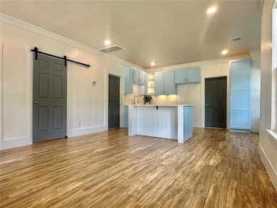 Kitchen featuring a barn door, light countertops, blue cabinets, ornamental molding, and light wood-type flooring