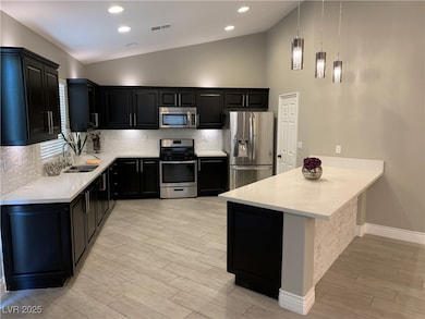 Kitchen with dark cabinets, stainless steel appliances, backsplash, light stone countertops, and vaulted ceiling