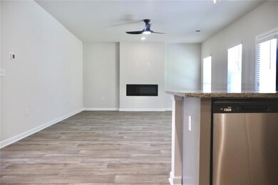 Kitchen featuring dishwasher, a ceiling fan, a glass covered fireplace, light wood-style flooring, and open floor plan
