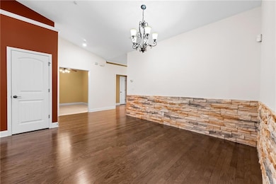 Unfurnished room featuring dark wood-style floors, vaulted ceiling, and a chandelier