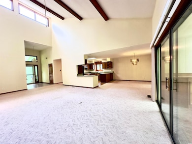 Unfurnished living room featuring a high ceiling, a chandelier, light colored carpet, and beamed ceiling