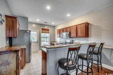Kitchen with appliances with stainless steel finishes, a peninsula, a textured ceiling, stone counters, and brown cabinetry