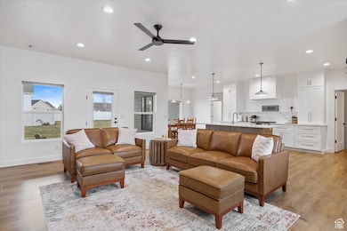 Living room featuring ceiling fan, baseboards, light wood-style flooring, and recessed lighting