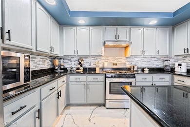 Kitchen featuring dark stone counters, appliances with stainless steel finishes, recessed lighting, decorative backsplash, and white cabinets