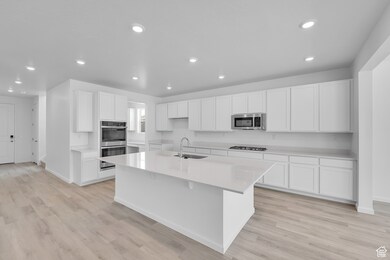 Kitchen with stainless steel appliances, recessed lighting, a kitchen island with sink, white cabinetry, and light countertops