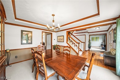 Dining room featuring a raised ceiling, crown molding, stairway, and a chandelier