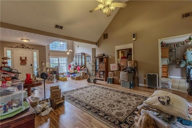 Living room with high vaulted ceiling, a ceiling fan, wood finished floors, a chandelier, and baseboards