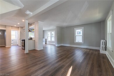 Unfurnished living room featuring ornate columns, brick wall, dark hardwood / wood-style flooring, and radiator heating unit