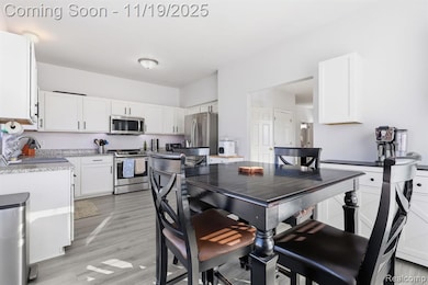 Kitchen featuring stainless steel appliances, white cabinetry, light wood finished floors, and light stone counters