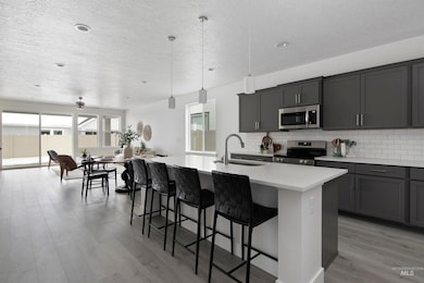Kitchen featuring decorative light fixtures, stainless steel appliances, backsplash, gray cabinets, and a breakfast bar