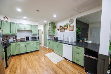 Kitchen with green cabinetry, open shelves, light wood-style flooring, stainless steel appliances, and glass insert cabinets