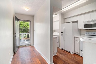Kitchen with white appliances, a textured ceiling, white cabinetry, washing machine and clothes dryer, and hardwood / wood-style floors