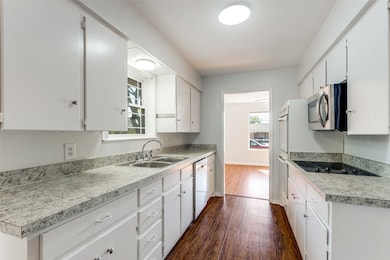 Kitchen featuring dark wood-style floors, white cabinetry, stainless steel microwave, and light countertops