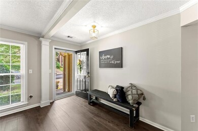 Entrance foyer with a textured ceiling, dark wood-style floors, crown molding, and ornate columns