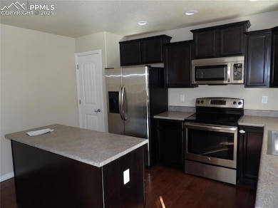 Kitchen with appliances with stainless steel finishes, light countertops, dark wood-style flooring, recessed lighting, and a kitchen island