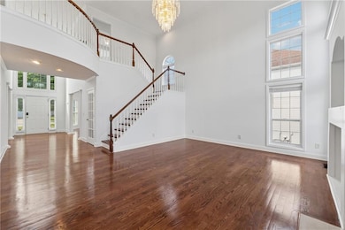 Unfurnished living room with a high ceiling, stairway, dark wood-style flooring, healthy amount of natural light, and a chandelier