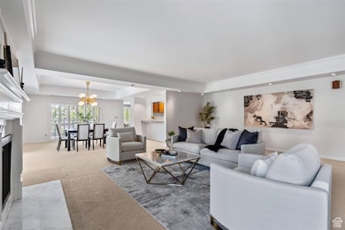 Living room with a fireplace with flush hearth, a tray ceiling, carpet flooring, a chandelier, and ornamental molding
