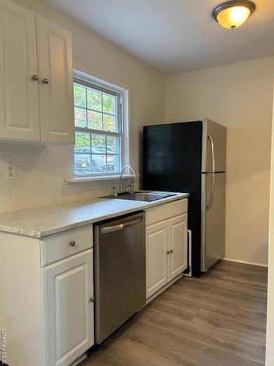 Kitchen with white cabinets, dark wood-style floors, dishwashing machine, and light countertops