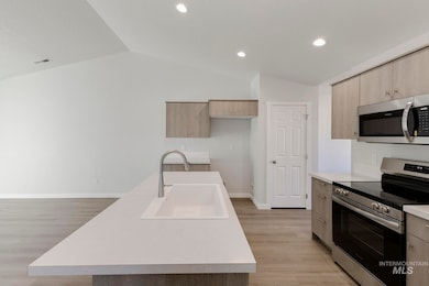 Kitchen featuring stainless steel appliances, light countertops, light wood-style floors, modern cabinets, and lofted ceiling