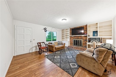 Living area with wood finished floors, a brick fireplace, built in shelves, a textured ceiling, and crown molding