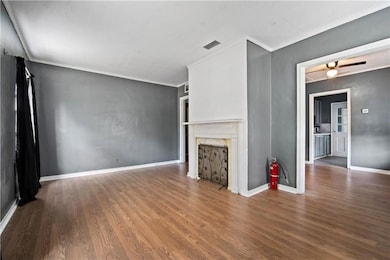 Unfurnished living room with wood finished floors, a fireplace, a ceiling fan, ornamental molding, and baseboards