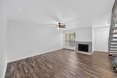 Unfurnished living room featuring a brick fireplace, dark wood finished floors, ceiling fan, and stairs