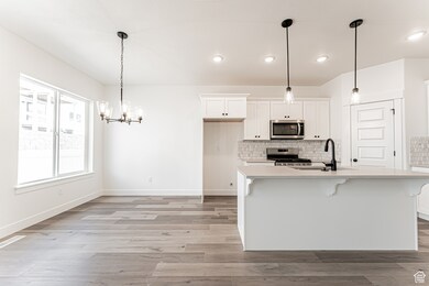 Kitchen with light countertops, appliances with stainless steel finishes, light wood-style flooring, white cabinetry, and tasteful backsplash