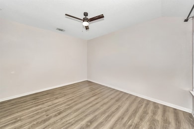 Empty room featuring wood finished floors, a textured ceiling, a ceiling fan, and vaulted ceiling
