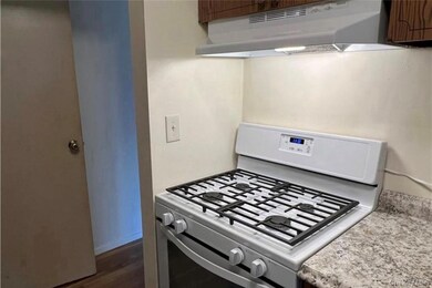 Kitchen with white gas range oven, under cabinet range hood, and dark wood-style flooring