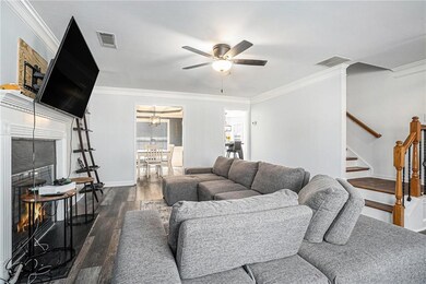 Living area with dark wood-type flooring, a ceiling fan, stairs, and crown molding