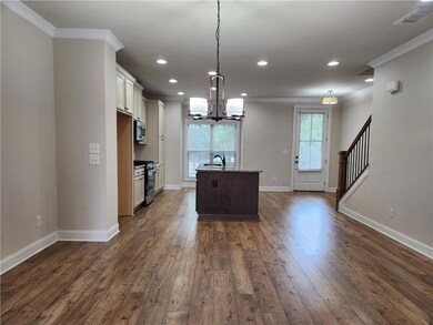 Kitchen with ornamental molding, dark wood-style floors, a chandelier, an island with sink, and appliances with stainless steel finishes