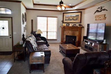 Tiled living area with ornamental molding, a ceiling fan, a tray ceiling, and a fireplace