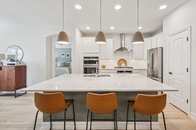 Kitchen with light wood look tile floors, a large island, light quartz counters, white cabinets, and pendant lights