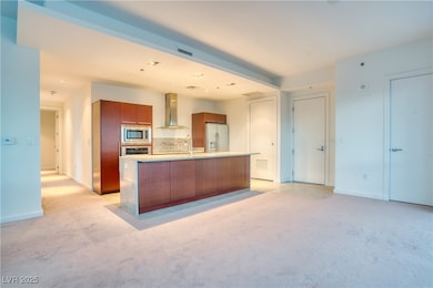Kitchen with light carpet, decorative backsplash, appliances with stainless steel finishes, wall chimney range hood, and a center island with sink