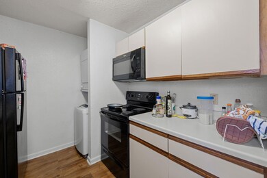Kitchen featuring black appliances, white cabinets, light countertops, a textured ceiling, and wood finished floors
