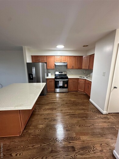 Kitchen featuring brown cabinetry, gas range, fridge, dark wood-style floors, and light stone countertops