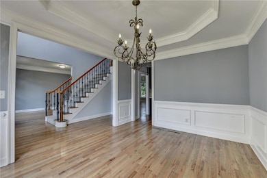 Unfurnished dining area with a chandelier, stairs, light wood-style floors, crown molding, and a raised ceiling