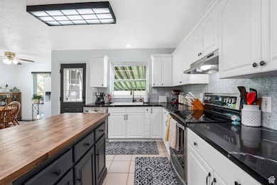 Kitchen with stainless steel range with electric stovetop, white cabinetry, tasteful backsplash, light tile patterned flooring, and under cabinet range hood