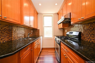 Kitchen with gas range, decorative backsplash, under cabinet range hood, dark stone countertops, and dark wood finished floors