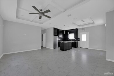 Unfurnished living room featuring ceiling fan, sink, a tray ceiling, and light tile floors