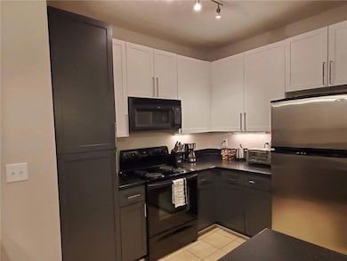 Kitchen with black appliances, dark countertops, white cabinets, and light tile patterned floors