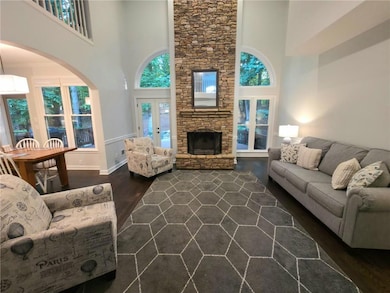 Living room with dark wood-type flooring, a towering ceiling, a stone fireplace, arched walkways, and french doors