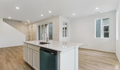 Kitchen with recessed lighting, dishwashing machine, an island with sink, light wood-style flooring, and white cabinetry