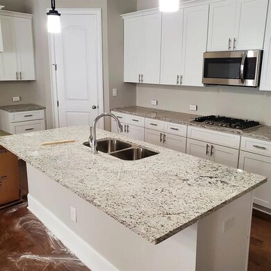 Kitchen with stainless steel appliances, a sink, white cabinets, and an island with sink