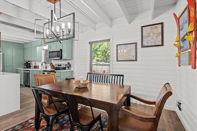 Dining room with dark wood-type flooring, a chandelier, beam ceiling, and wood walls