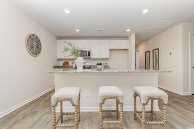 Kitchen featuring stainless steel microwave, light wood-type flooring, a center island with sink, a breakfast bar area, and recessed lighting