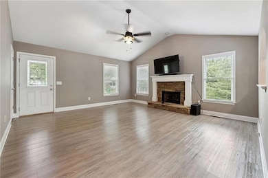 Unfurnished living room featuring a ceiling fan, a fireplace, light wood-type flooring, and lofted ceiling