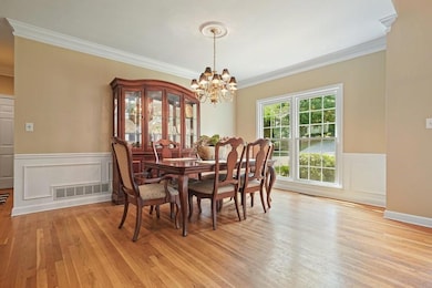 Dining area with ornamental molding, a chandelier, light wood-style floors, a wainscoted wall, and a decorative wall