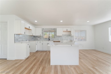 Kitchen with tasteful backsplash, white cabinets, light wood finished floors, recessed lighting, and a kitchen island