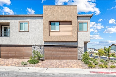 View of back of house featuring stone siding, a garage, decorative driveway, and stucco siding